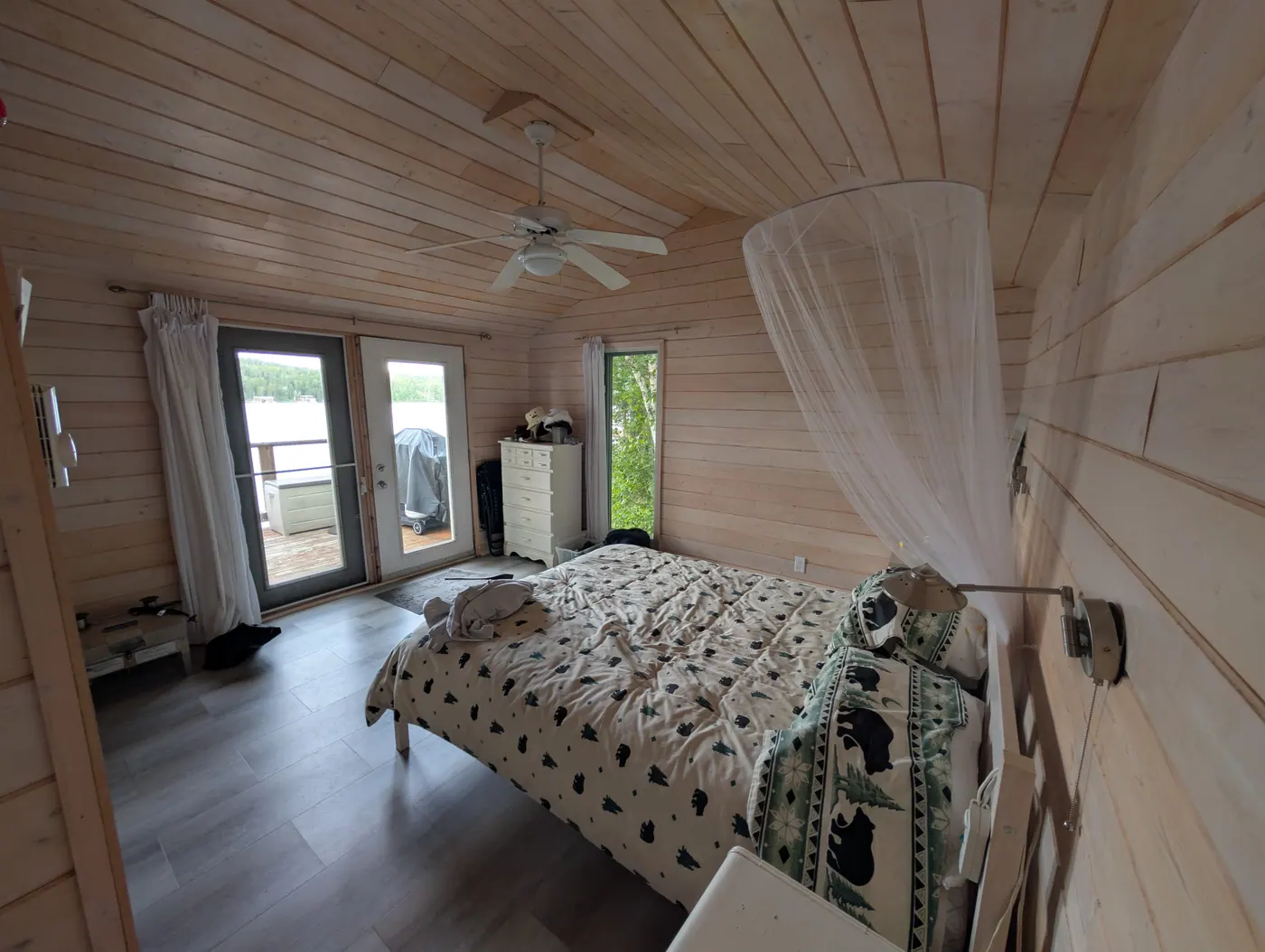 A bedroom with pine ceiling and doors opening toward the water.