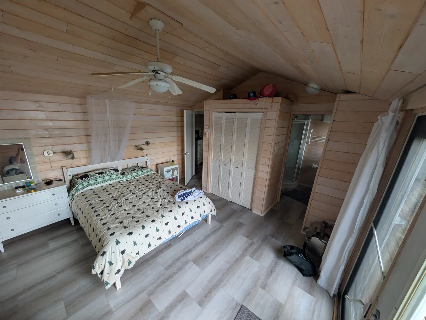 A second bedroom under the pine ceiling, with morning light.