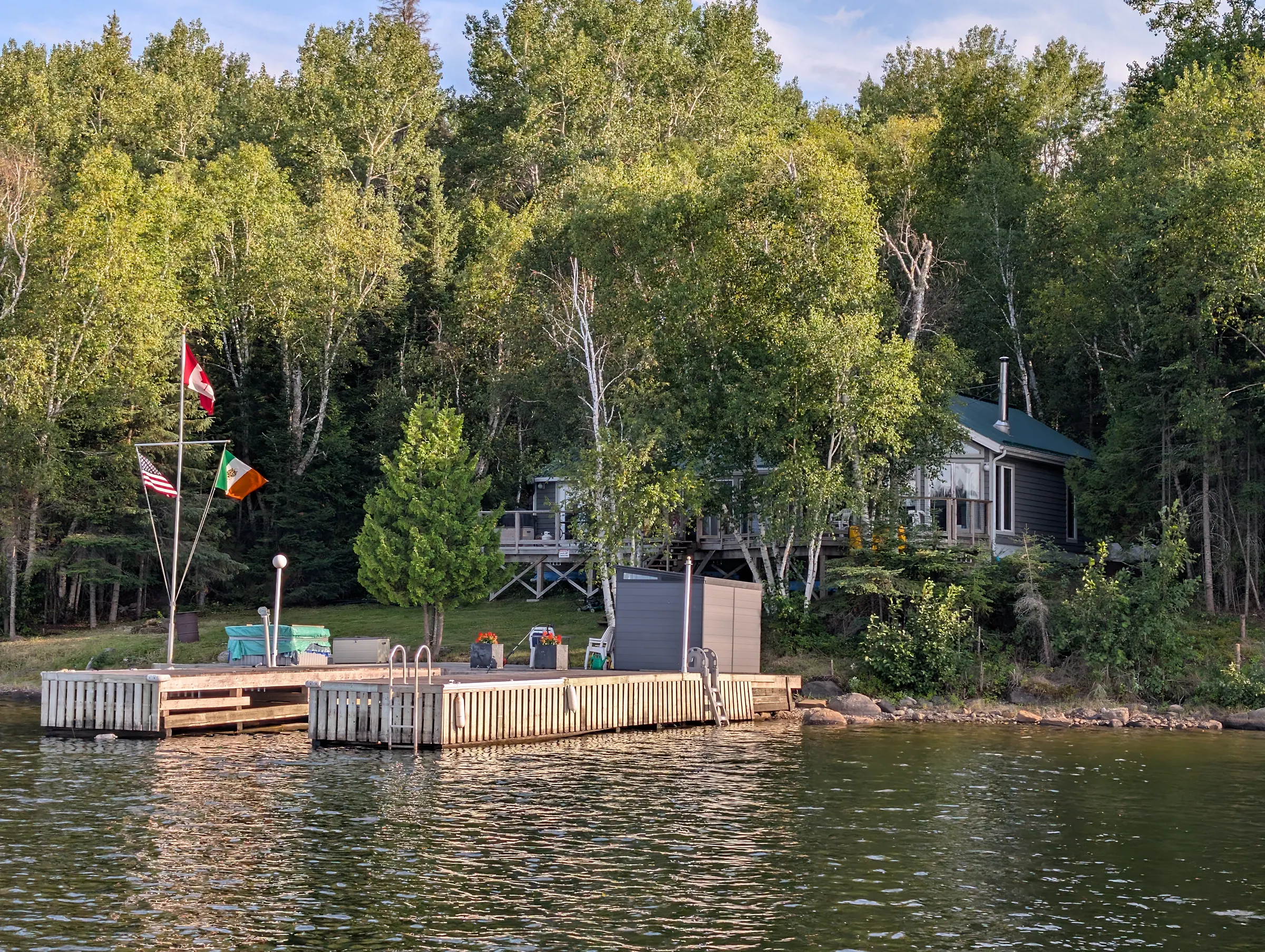The property seen from the water at Woodchuck Bay: the dock along the shoreline, birches and evergreens behind, and the cottage among the trees.
