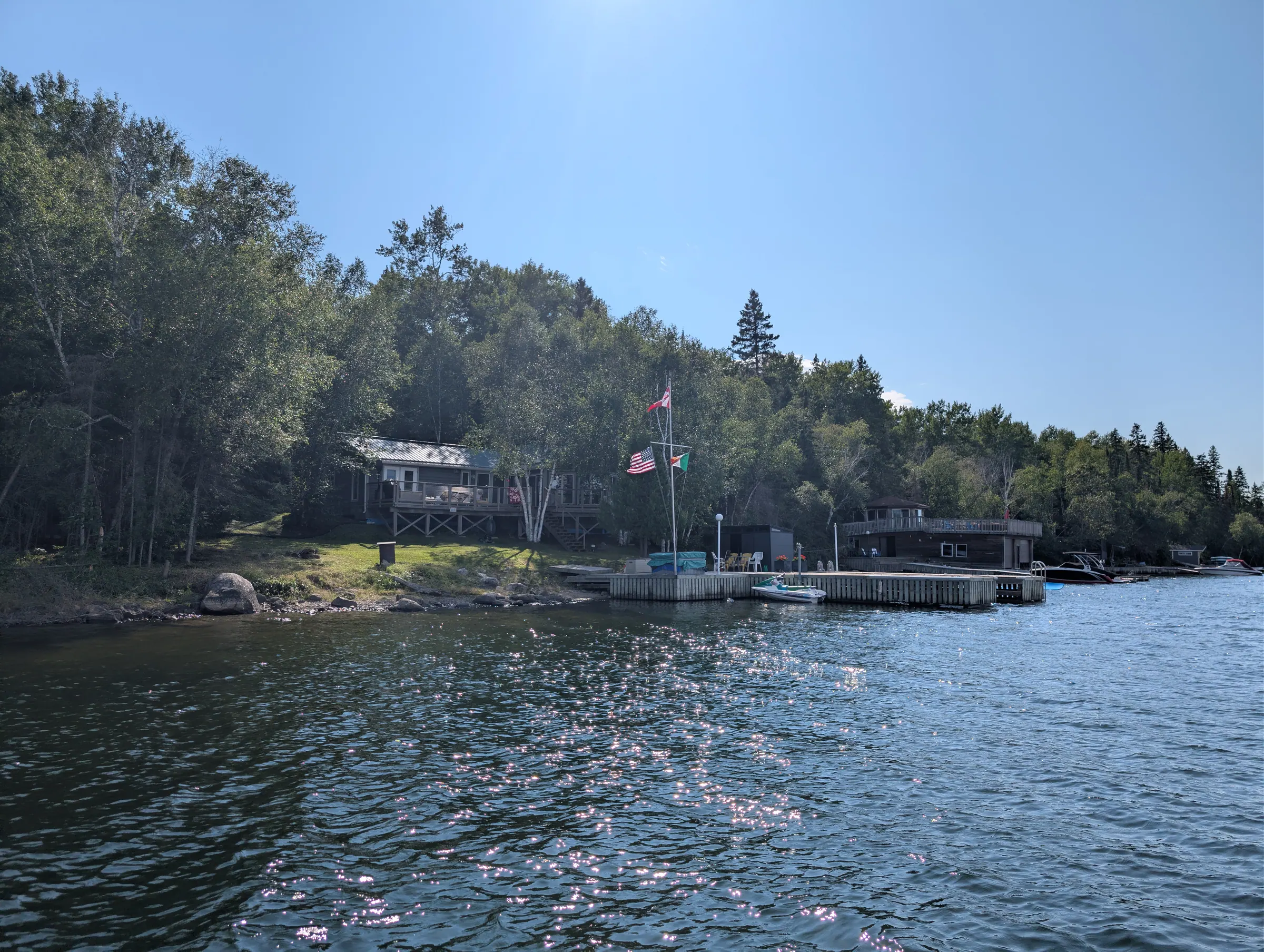 The shoreline of the property seen across the water, the dock running along its front edge.