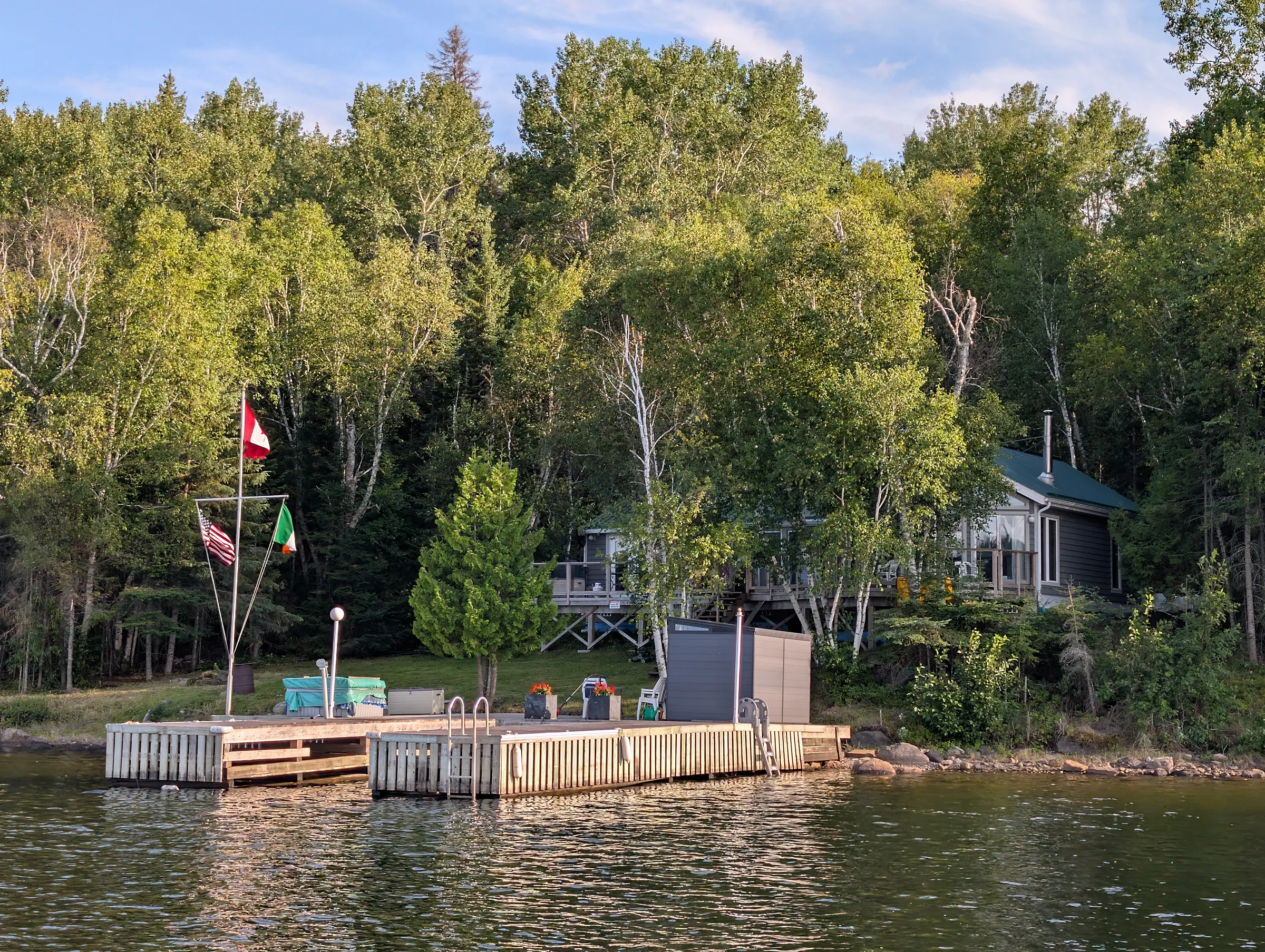 The point from the water in late light, the cottage visible among birches above the dock.