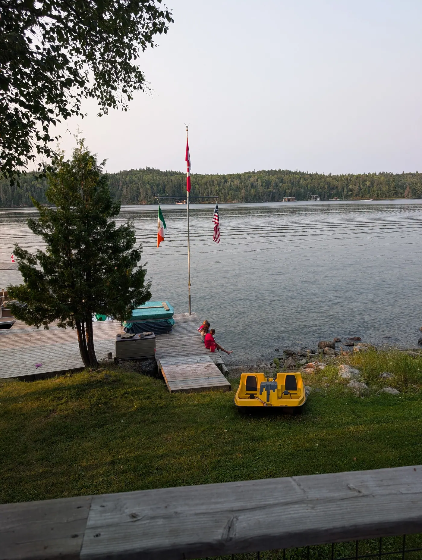 The waterfront with flags flying and a canoe pulled up on the shore.